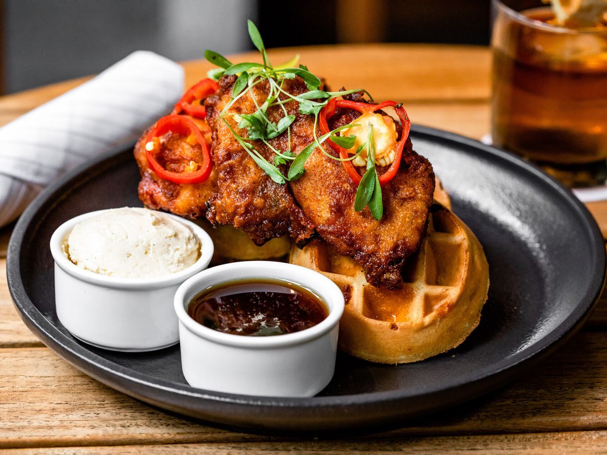 Fried chicken atop a waffle, served with a side of whipped butter and bourbon maple syrup at Bayou &amp; Bottle in the Four Seasons.