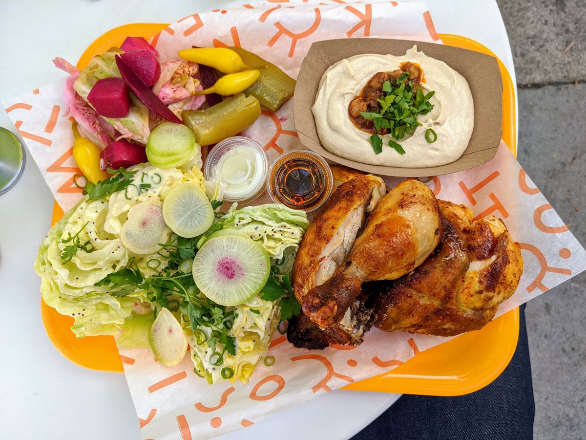 A tray full of roast chicken, hummus, a green salad, and pickled vegetables at Kismet Rotisserie.
