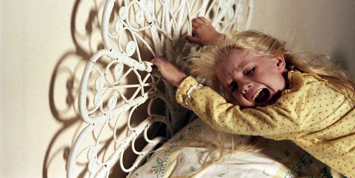 A little girl clings to her bedframe, screaming, as something offscreen tries to pull her away.