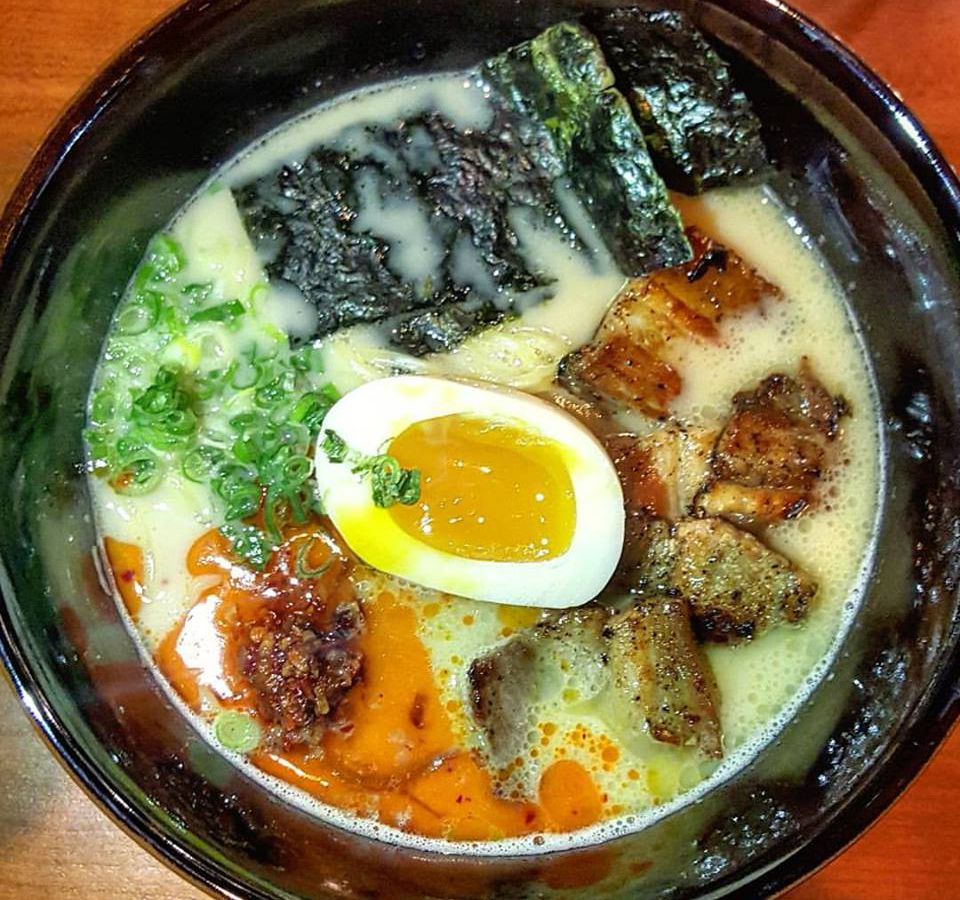 Overhead shot of a bowl of ramen with a creamy pale yellow broth, chile oil, soft boiled egg, seaweed, scallions, and crispy pork