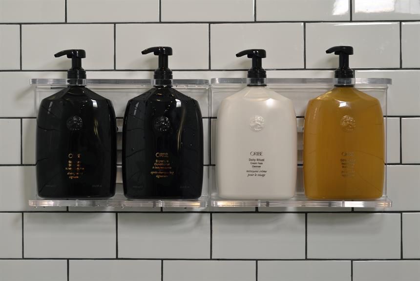 Four bottles of Oribe products against a tile wall. 