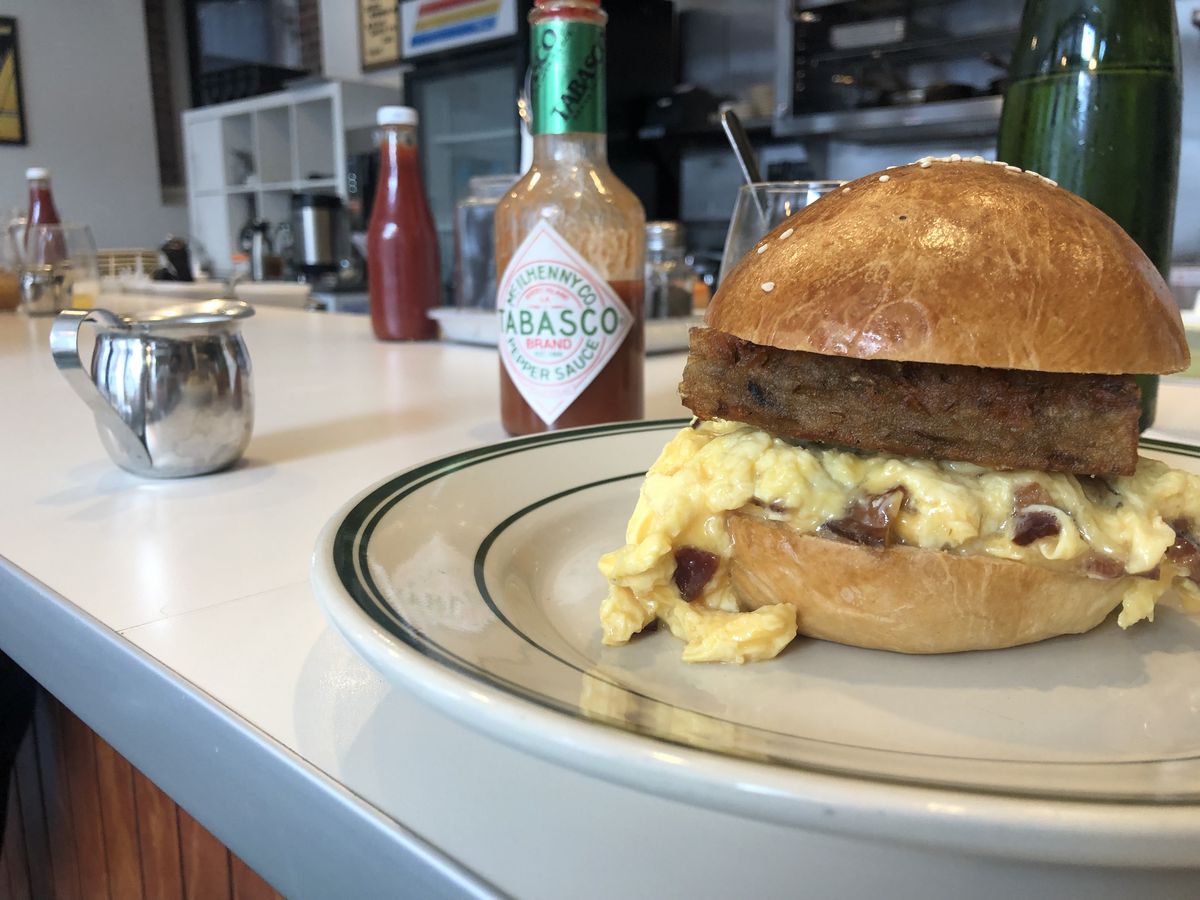 An fluffy egg sandwich with pieces of bacon and a thick hash brown patty rests on a diner plate.