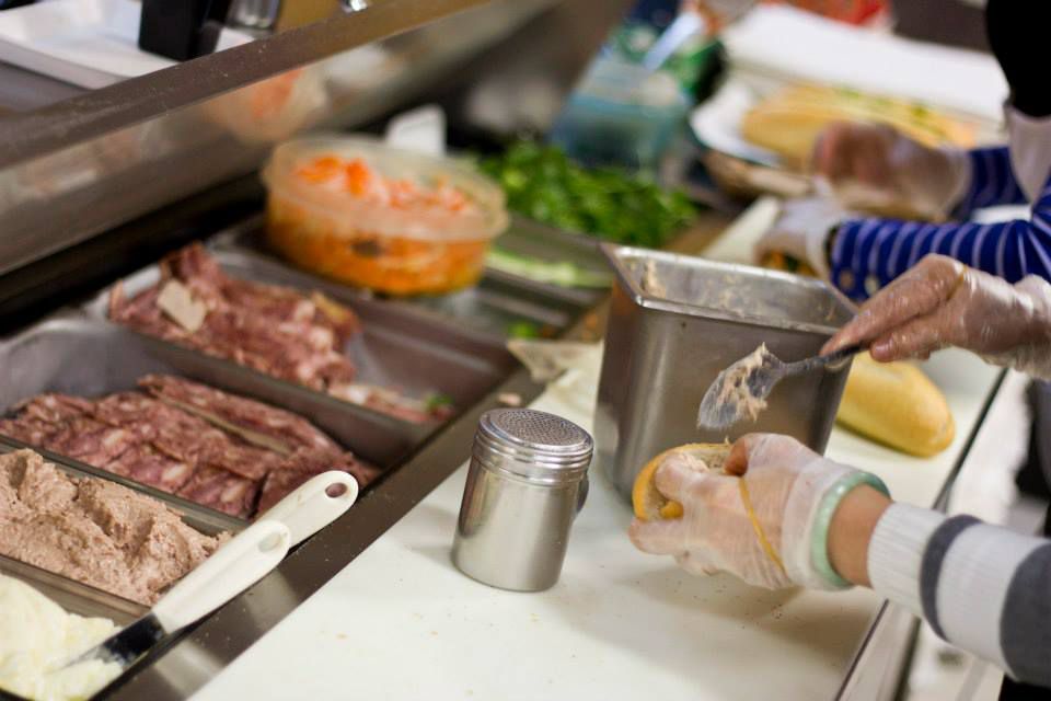 A station of cold cuts and condiments with a worker slathering on dressing