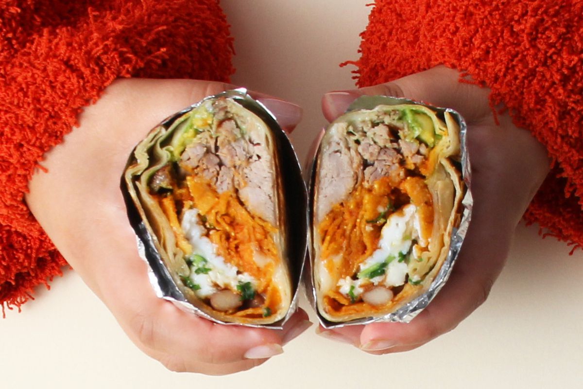 Two hands hold a burrito from Los Burros Supremos.