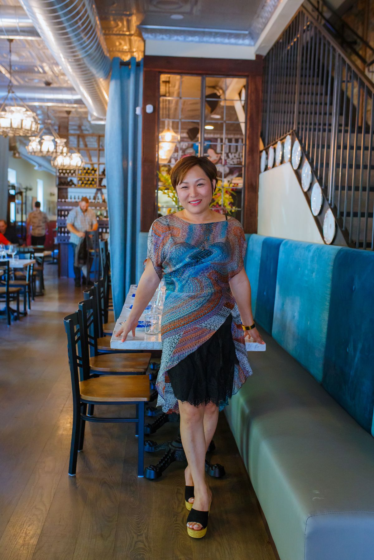 A woman in a colorful dress stands inside a restaurant with wooden floors.