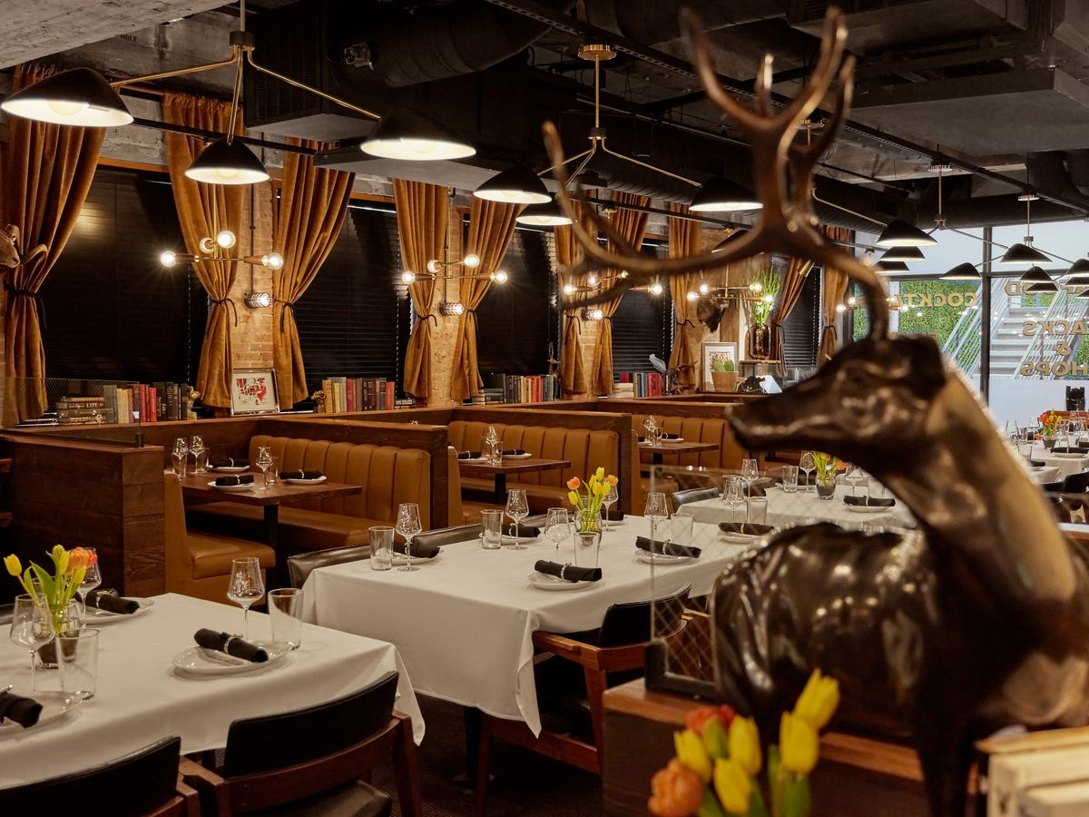 A steakhouse dining room features white cloth covered tables, gold curtains, soft lighting, an in the foreground, a brass ram.