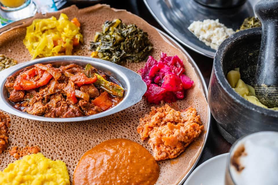 A bowl of meat sits in a piece of injera surrounded by sauteed vegetables. 