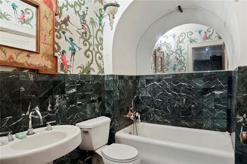 A bathroom with green tile and hideous wallpaper. 
