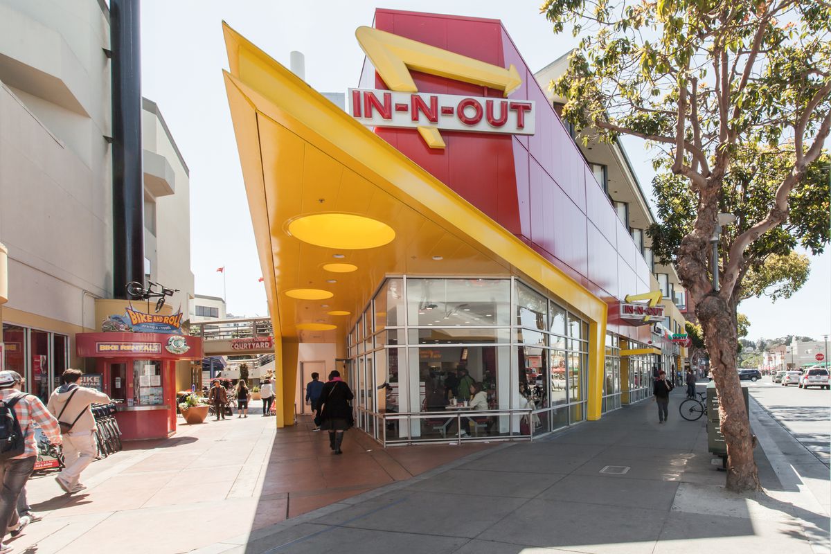The front door of In-N-Out Burger at Fisherman’s Wharf, including the restaurant’s yellow, triangular awning and iconic yellow, red, and white sign.