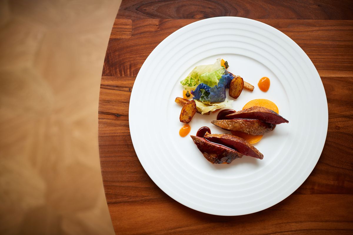 Pieces of roast pigeon, plated with vegetables and fruits.