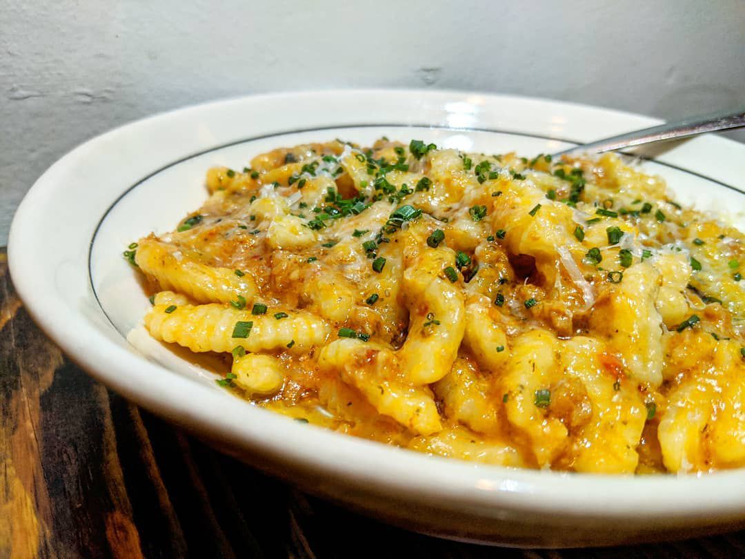 A white bowl of cavatelli in an orange-ish sauce sits on a wooden table
