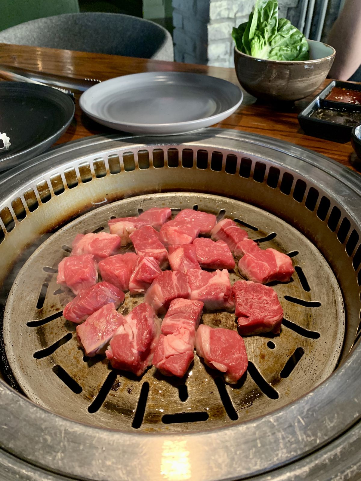 A Korean grill set inside a wooden table is filled with pieces of raw beef.