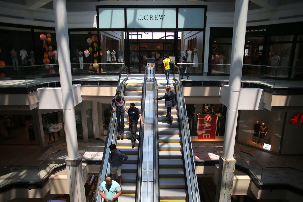 A wide shot of a pair of mall escalators in an airy mall with shops visible; and there are people on the escalators. 