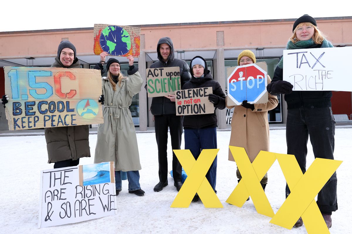 Protesters stand holding signs about climate change in front of a building. 