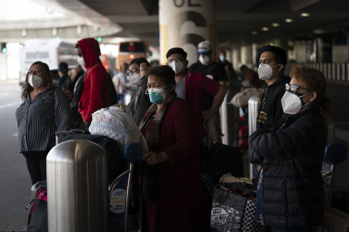 Travelers wait for a shuttle but to arrive at the Los Angeles International Airport in Los Angeles, Monday, Dec. 20, 2021. The Los Angeles County Department of Public Health reported more than 3,500 new cases of COVID-19 on Sunday as the number of daily new cases tripled over the week.