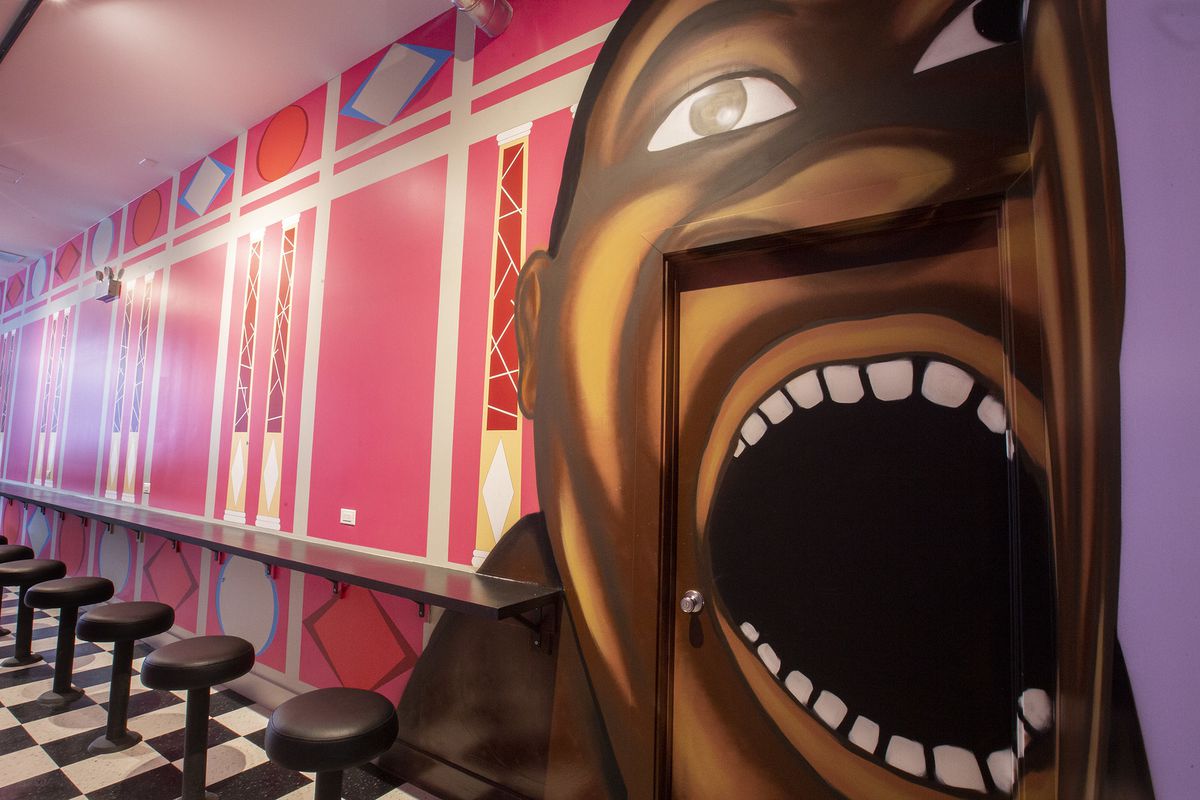 A pink wall painted with geometric designs and a mural of a face with a large open mouth.