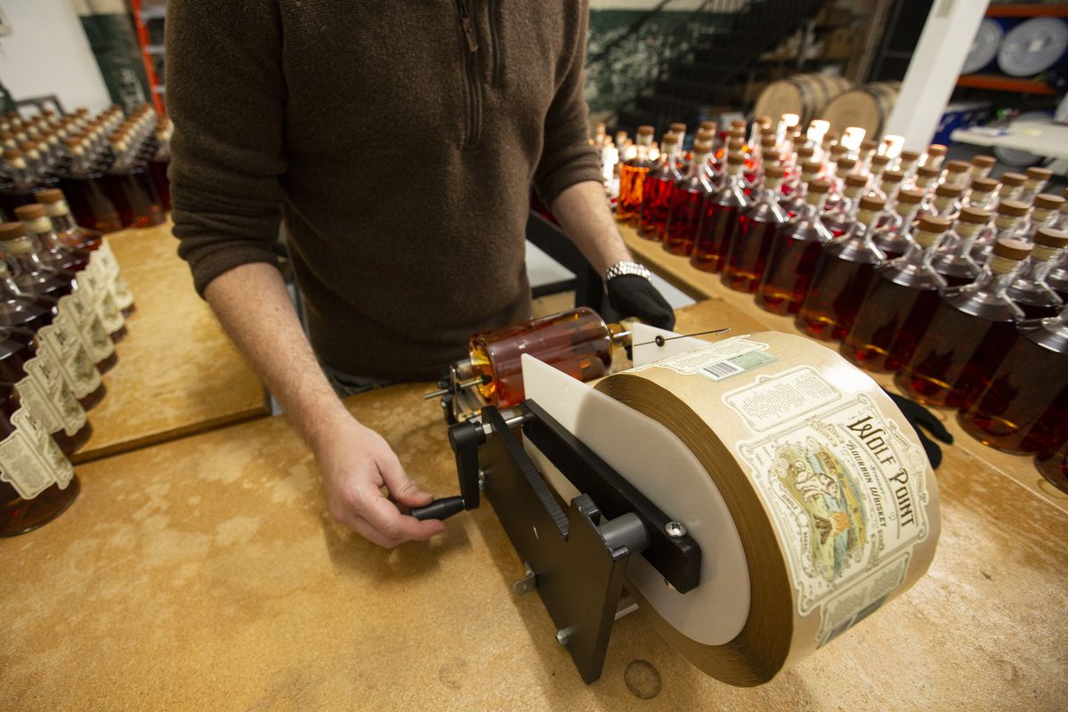 A person uses a rolling contraption to wrap a label around a bottle.