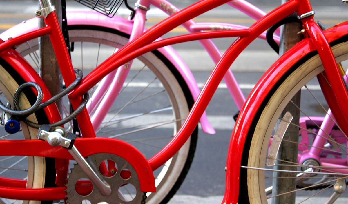 Two bicycles next to each other. One bicycle is red and the other bicycle is pink.