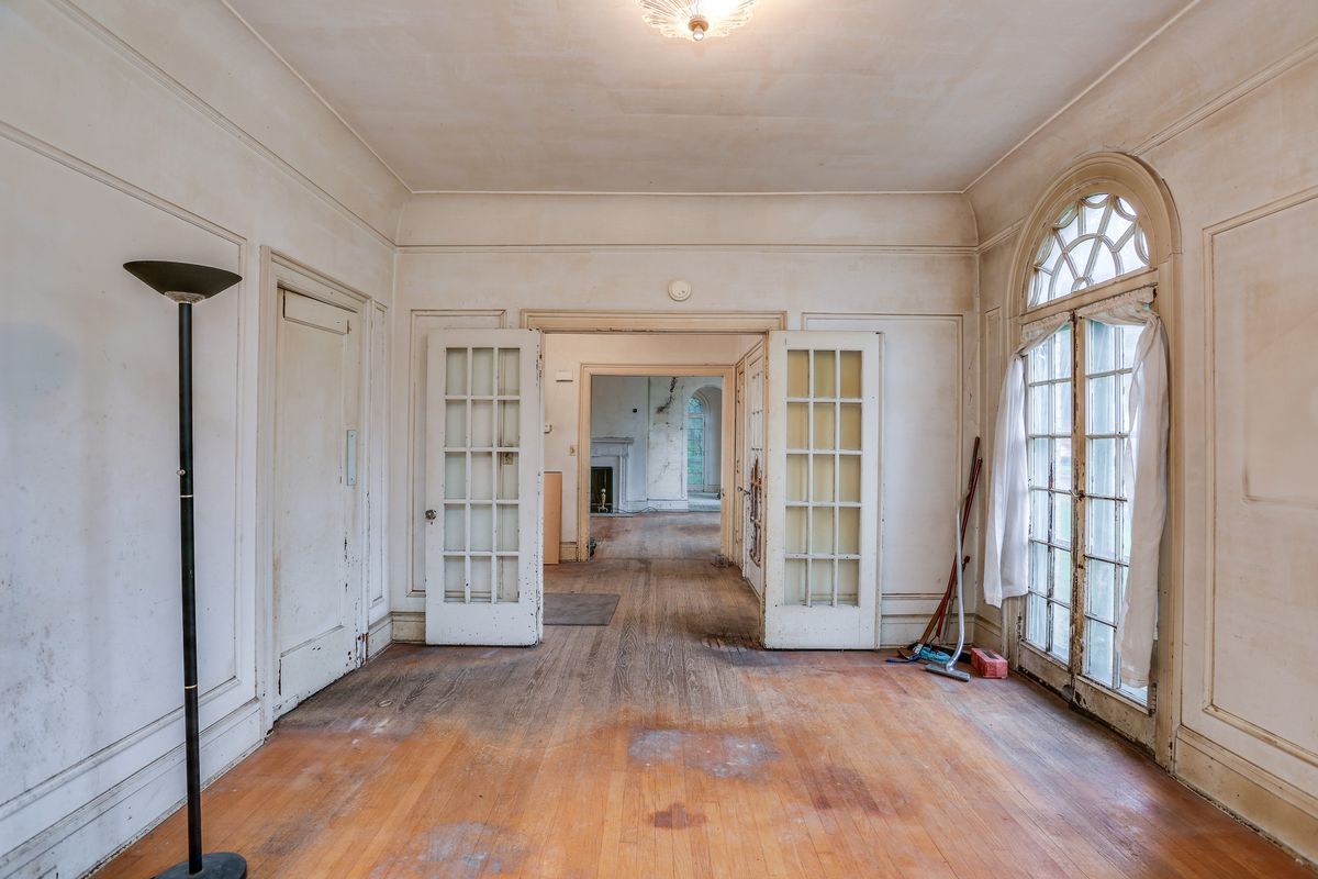 A view of an empty den with white walls. Doors are open in several consecutive rooms so you can see down the length of the home. Again, the floors are discolored in numerous places. 