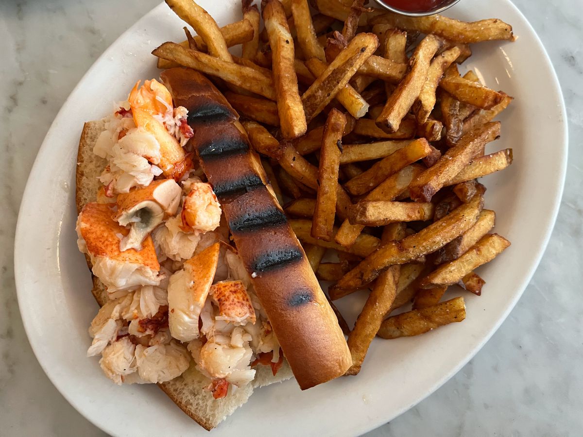 An overhead photo of a lobster roll with a grilled hot dog bun and a pile of fries on the side.
