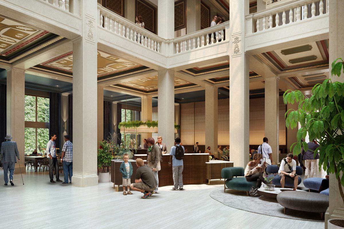 People sit on low couches near planters and wait at a desk area in the lobby. There’s tall columns that connect to the second floor.
