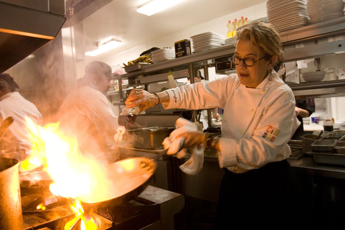 A woman cooking something in a pan with a lot of fire. 