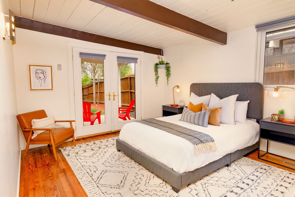 A gray bed sits on a gray and white rug in a bedroom with exposed beams. 