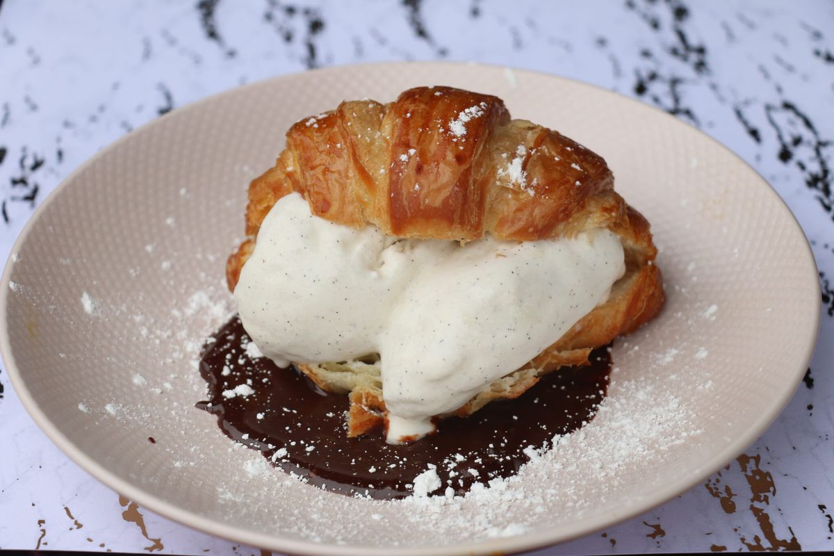 A croissant with vanilla ice cream on chocolate sauce on a plate. 