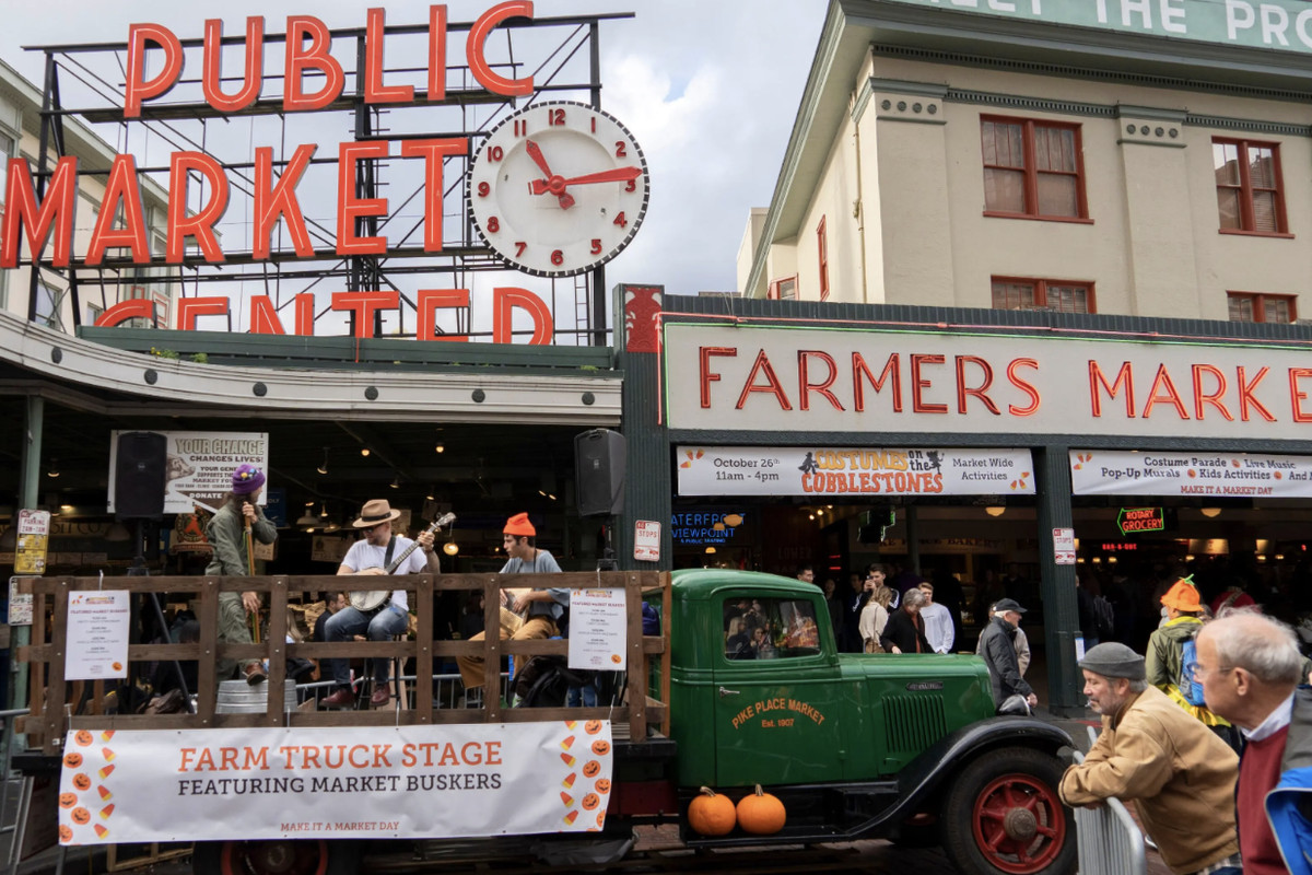 Three musicians playing on the back of and old-school green pickup truck in front of Pike Place Market’s famous red “Public Market” sign.