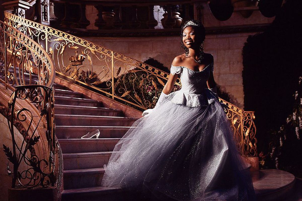 Brandy, dressed in a ballgown and tiara, steps down a sweeping staircase.