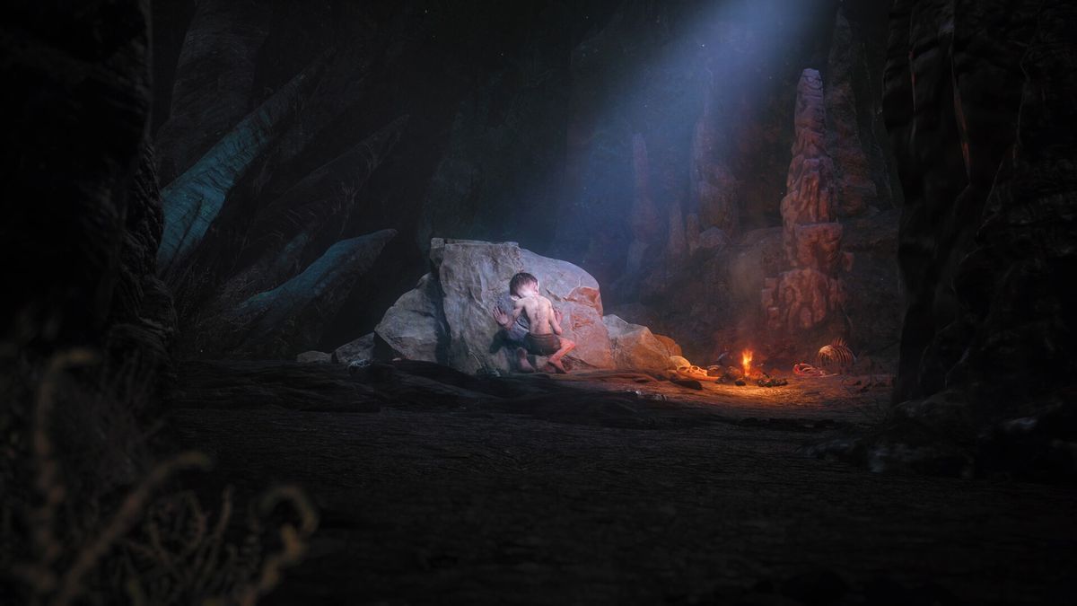 In a dark cave lit by a small fire and a beam of light from the sky, Gollum crouches with his back to the “camera,” scrawling on a flat rock.