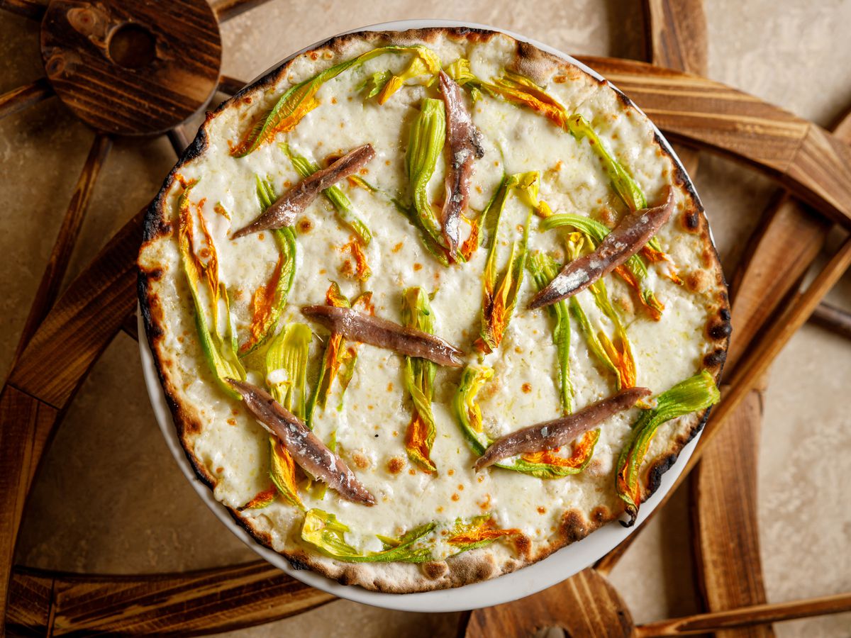 From above, a white pizza with long strands of zucchini flower and anchovies.