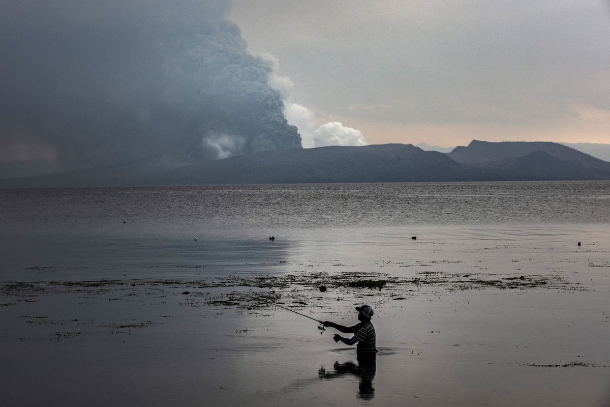 A resident fishes at a lake as Taal Volcano erupts on January 13, 2020 in Balete, Batangas province, Philippines.