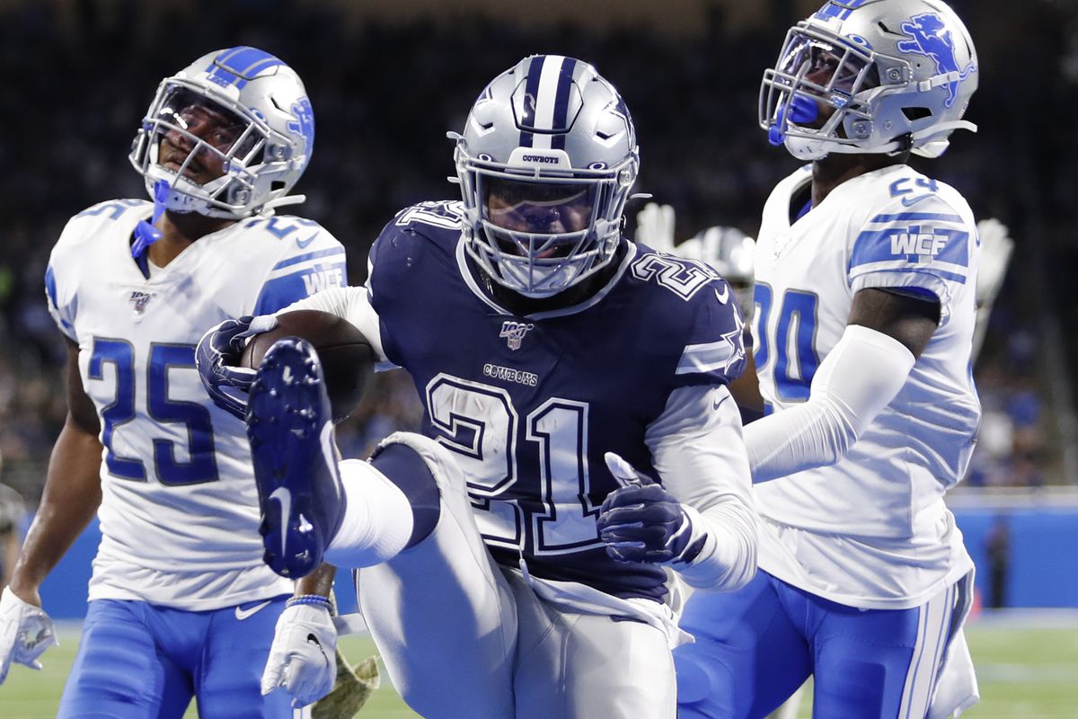 Dallas Cowboys running back Ezekiel Elliott high steps into the end zone with a rushing touchdown in front of Detroit Lions defensive back Will Harris  and cornerback Amani Oruwariye during the fourth quarter at Ford Field.