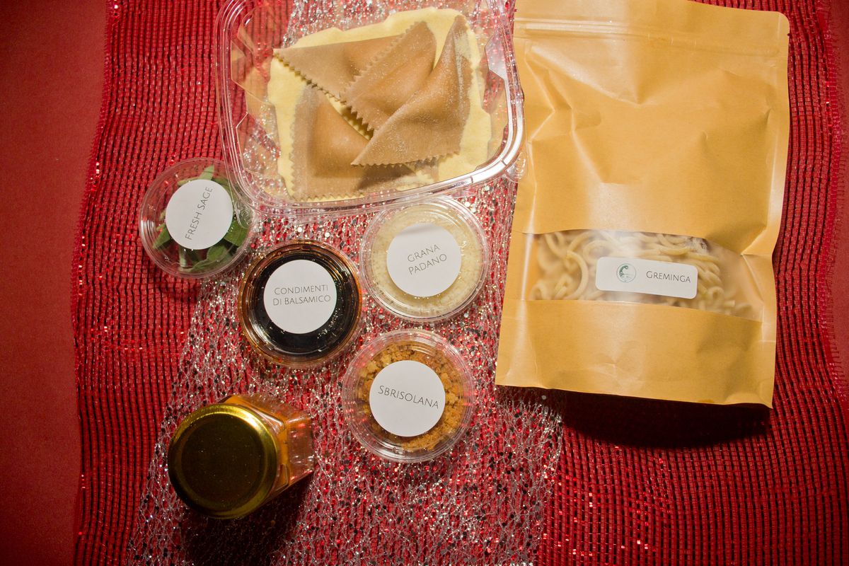 A plastic container of ravioli pasta, a light brown bag with a clear window of pasta, plastic containers, and a jar. 