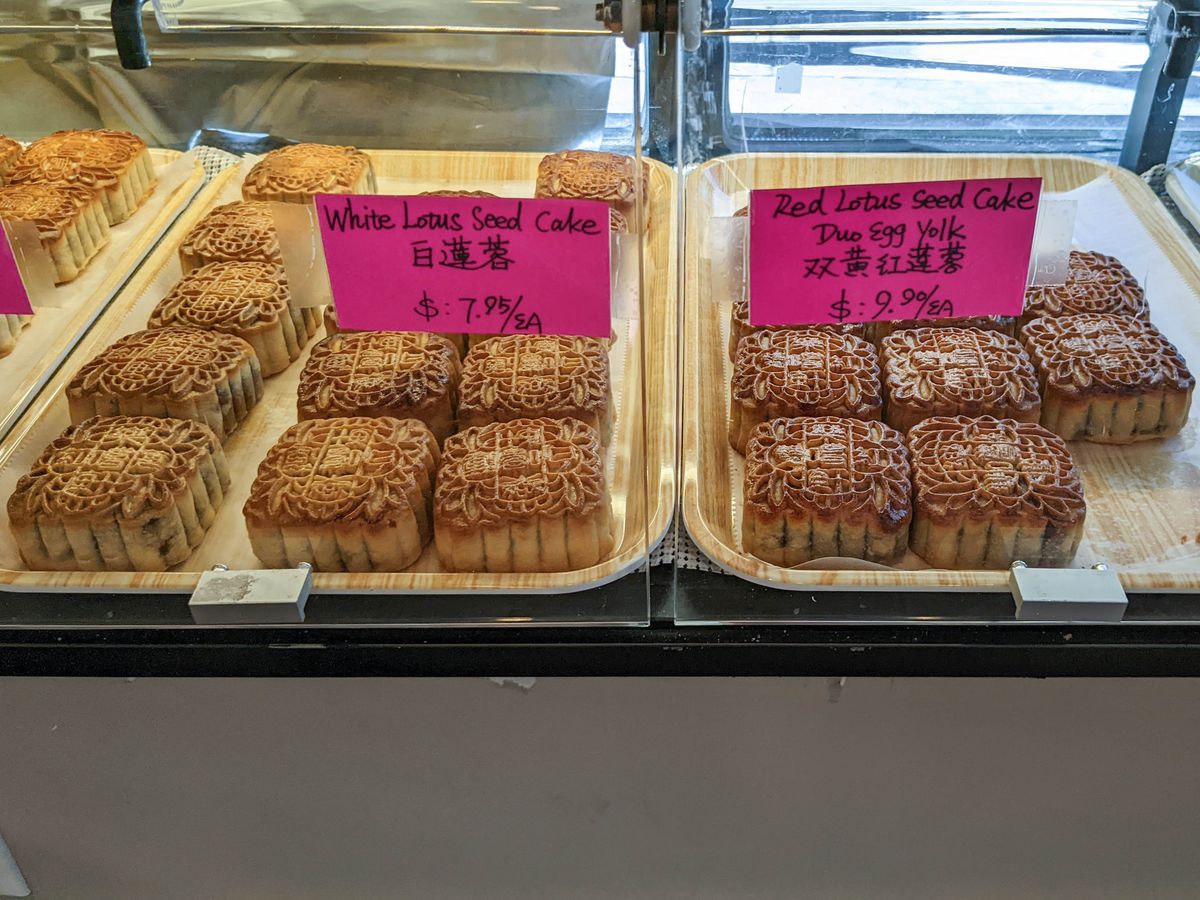 Square, intricately decorated mooncakes with a golden-brown crust are on display in a pastry case.
