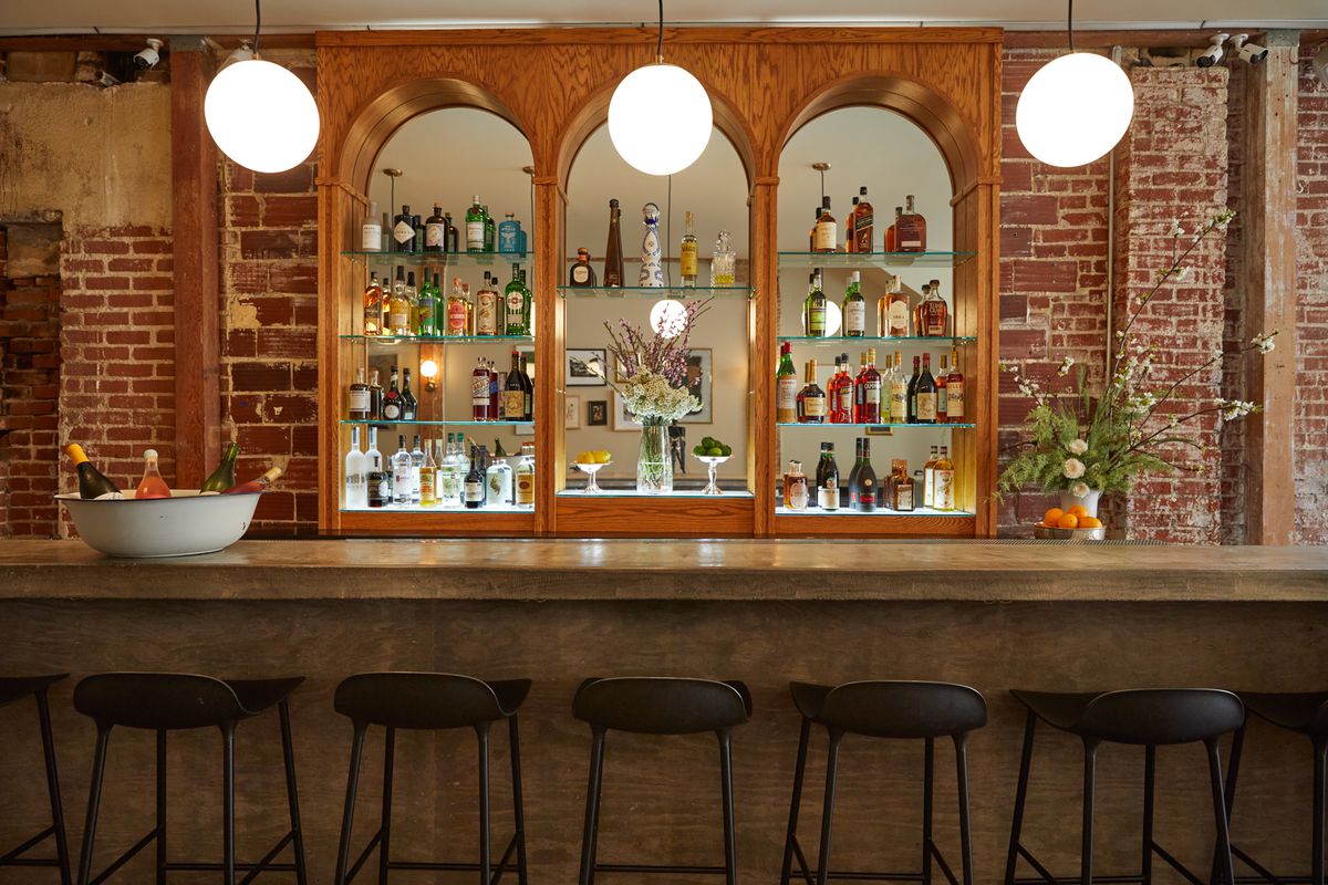 Bar avec murs en briques apparentes, tabourets et dos voûtés avec des bouteilles d'alcool au restaurant Coucou à Venise, en Californie.