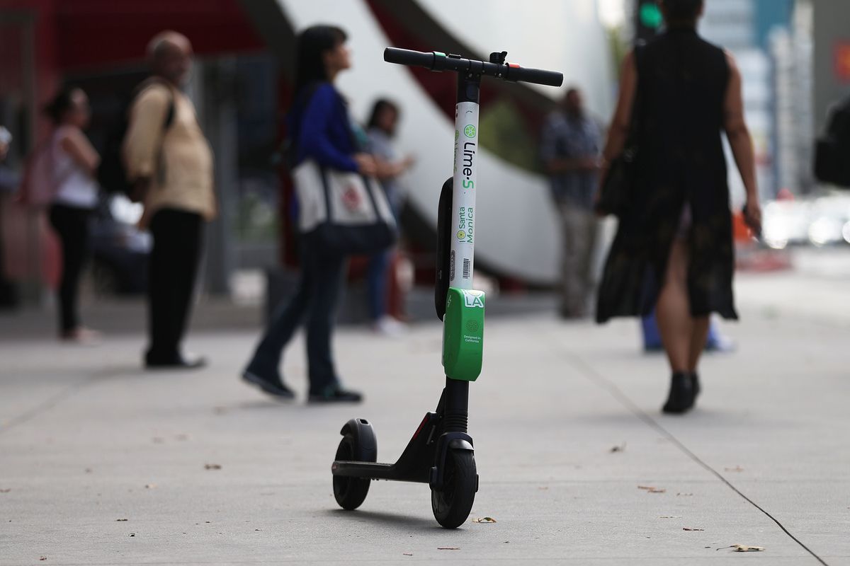A Lime dockless electric scooter parked on a street with people walking by