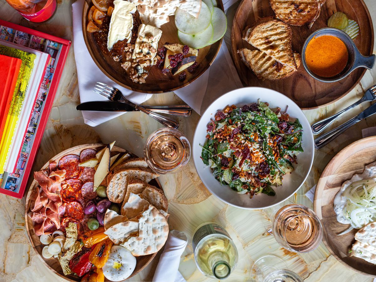 A spread of salads, charcuterie board, grilled cheese, and glasses of wine at Postino.