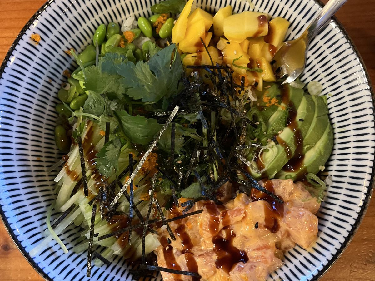 A closeup on a bowl of fish and vegetables, divided into portions, presented in a patterned bowl. 