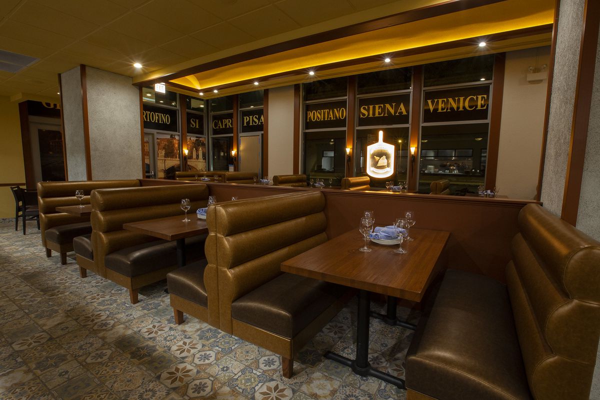 Brown leather booths with tables with plates, glasses, and napkins; in the background, windows with the names of Italian cities in the top panels