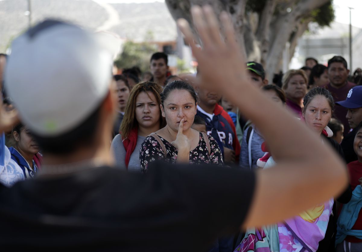 In this June 13, 2018 photo, an organizer speaks to families as they wait to request political asylum in the United States, across the border in Tijuana, Mexico. In Tijuana, Latin Americans fleeing drug violence in their countries are camped out and waiti