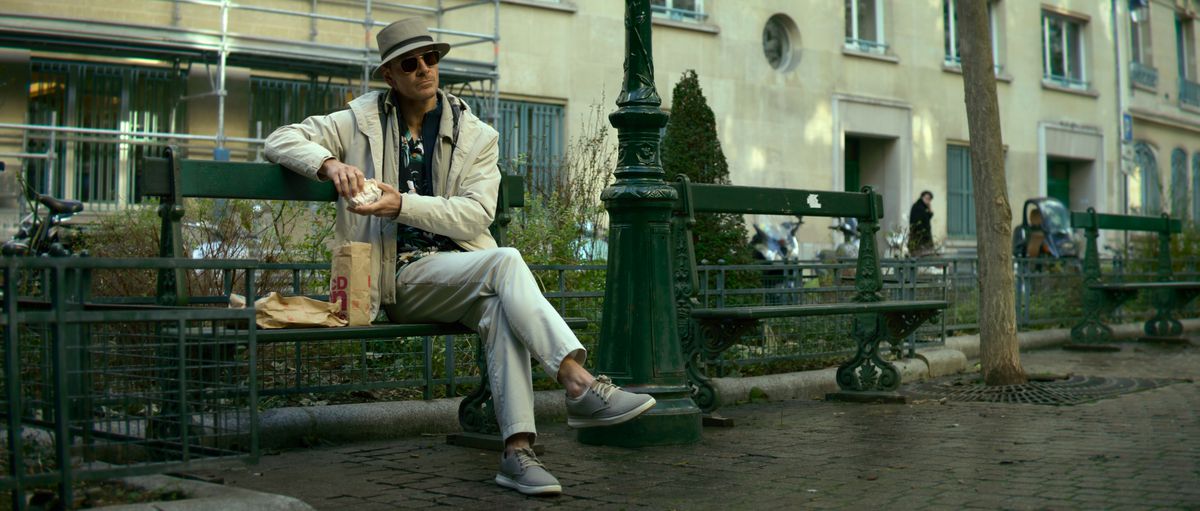 Michael Fassbender as an assassin sitting on a bench and eating a McMuffin in The Killer.