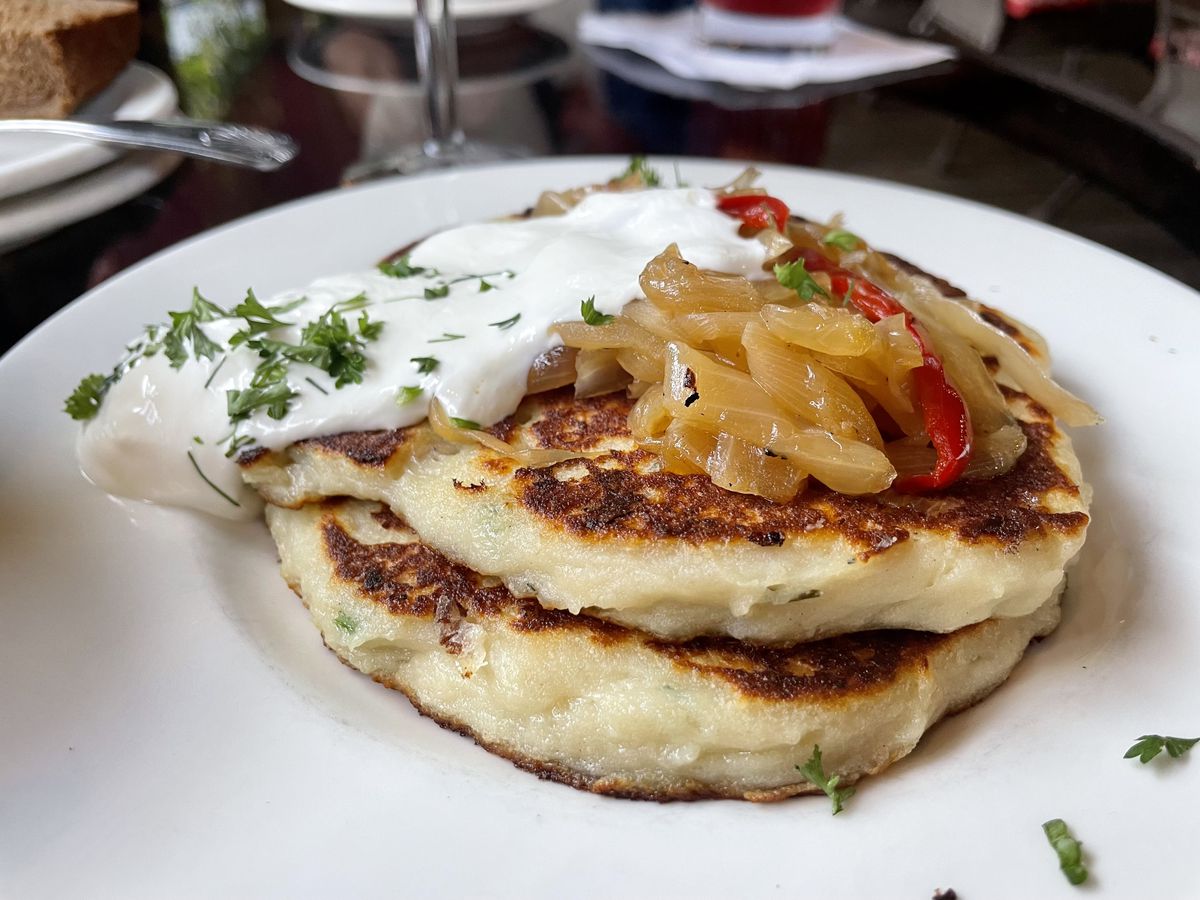 Two potato pancakes on a white plate topped with sour cream and caramelized onions. 