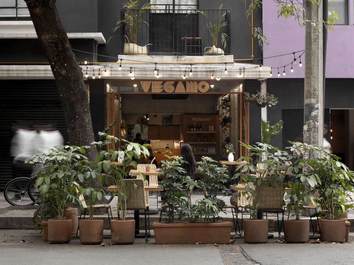 A restaurant exterior veiled in sidewalk plants and string lights. 