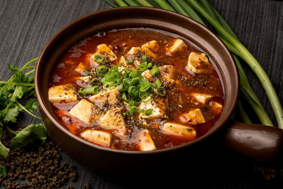 A bright red bowl of mapo tofu loaded with spices.