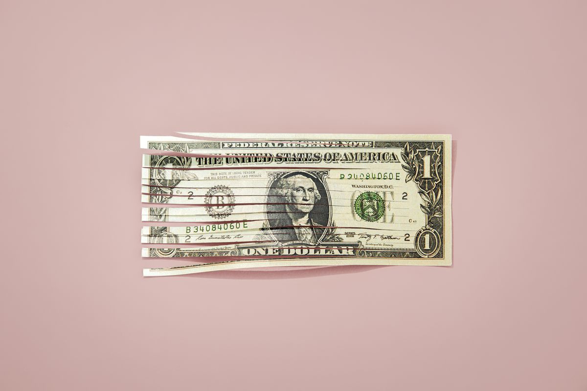 An image of a shredded dollar bill against a pink background.