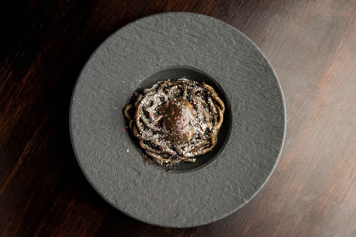 An overhead shot of a black pasta with coddled egg in a slate bowl with wide rim.