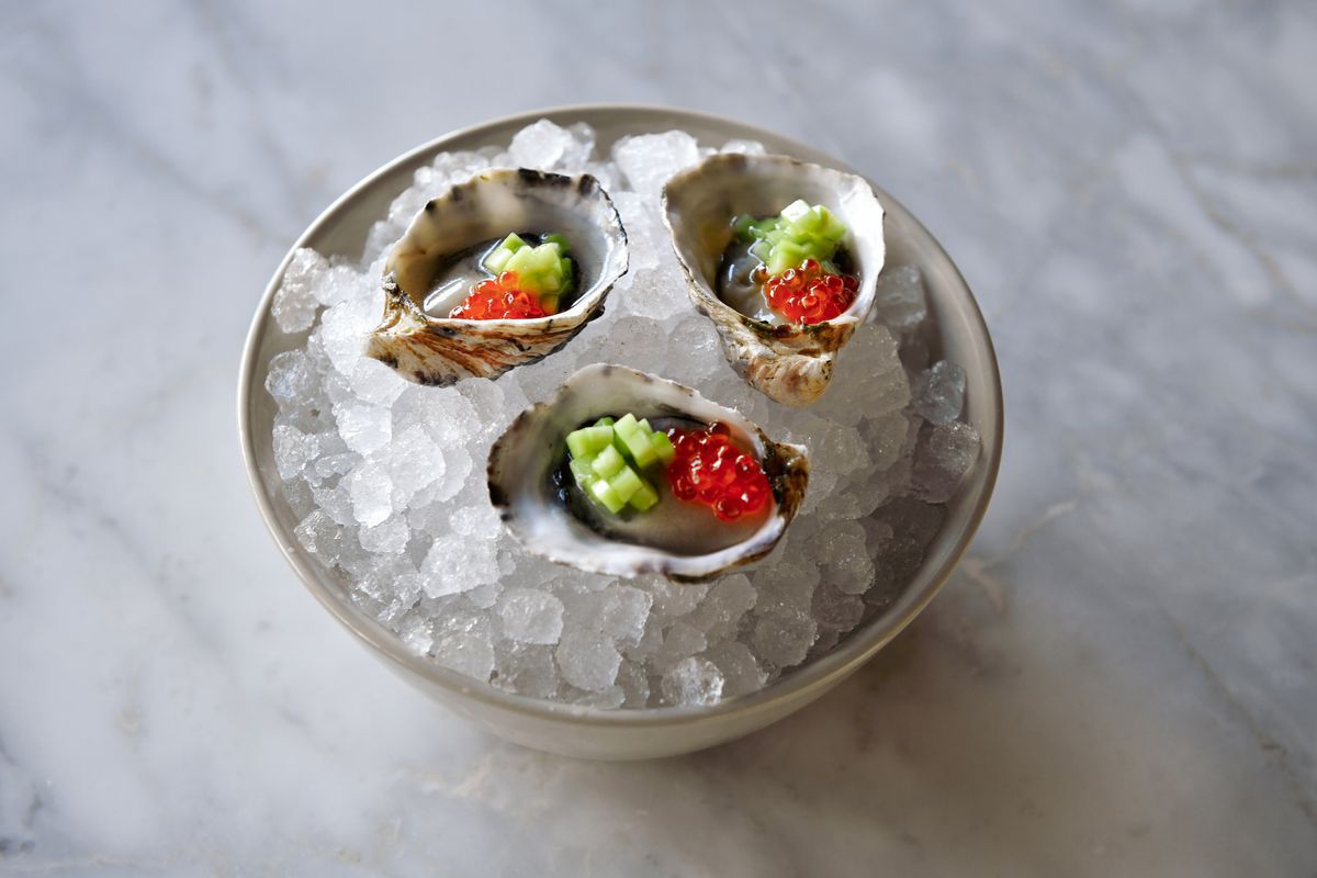 Three oysters in a bowl of ice with roe and chops of cucumber.