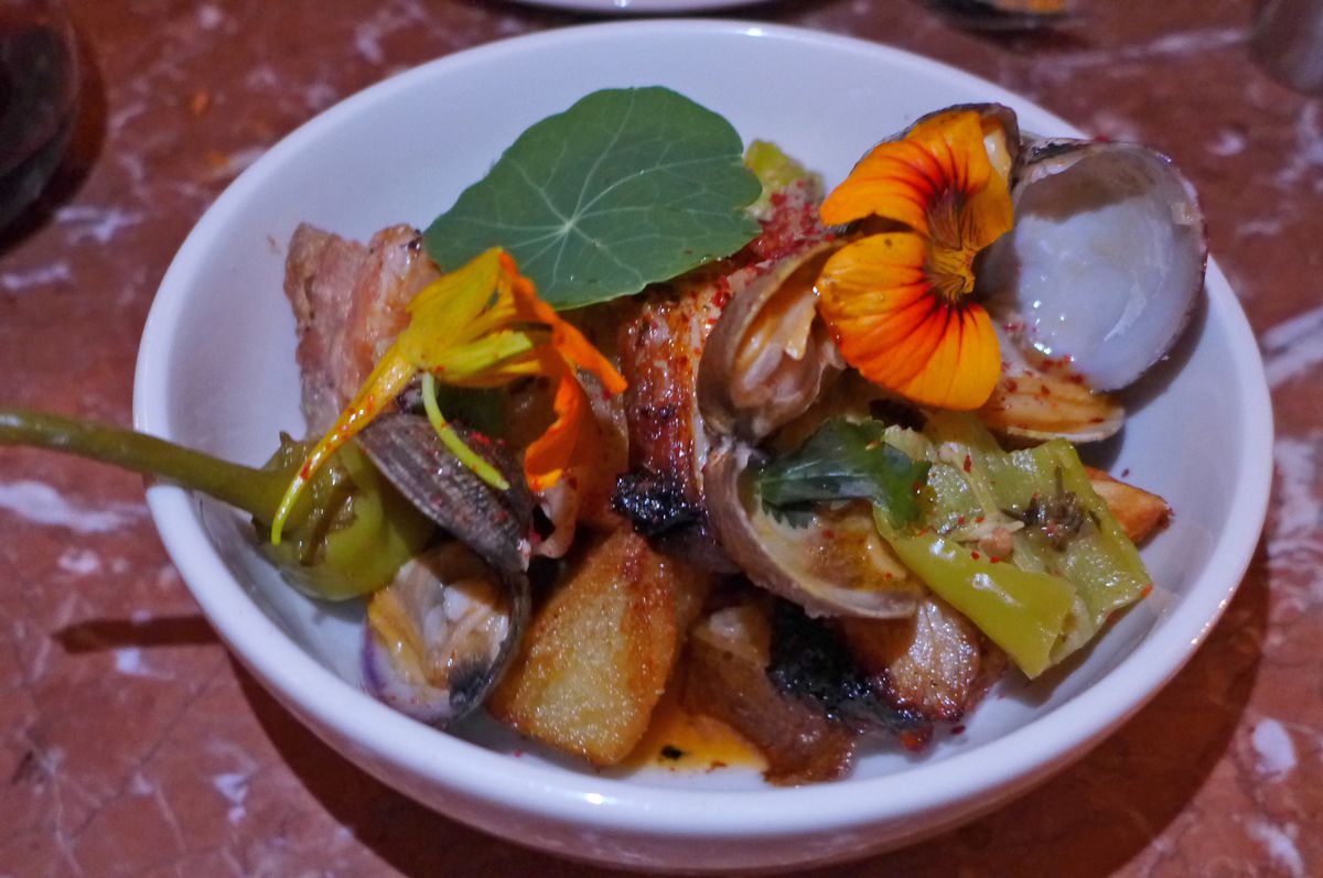 A smalls bowl of clams in their shells, pork belly, and nasturtium flowers and leaves.